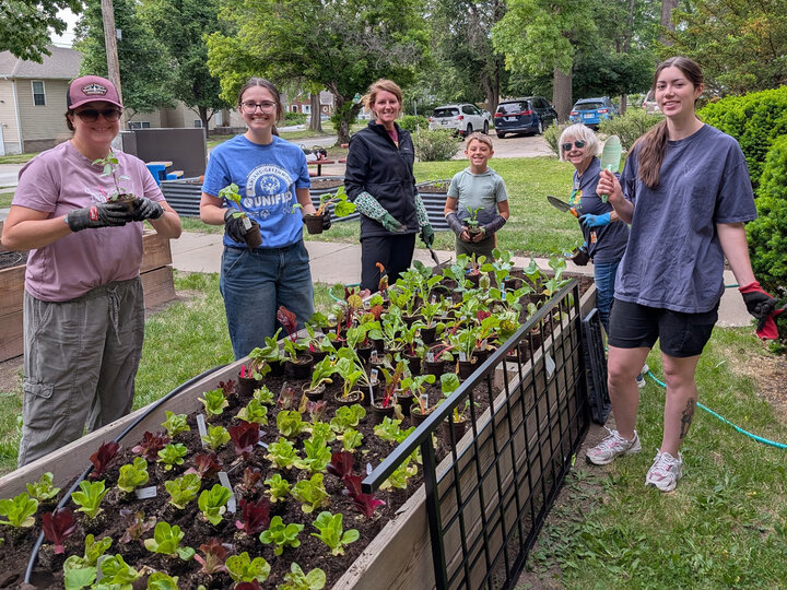 Group gardening near a raised garden bed filled with leafy plants, surrounded by greenery.