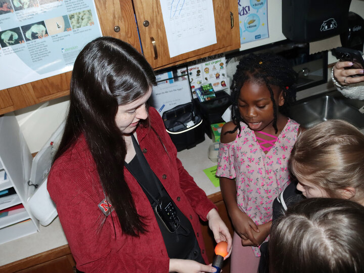 Woman holding an egg up to a flashlight as three girls look at the glowing egg