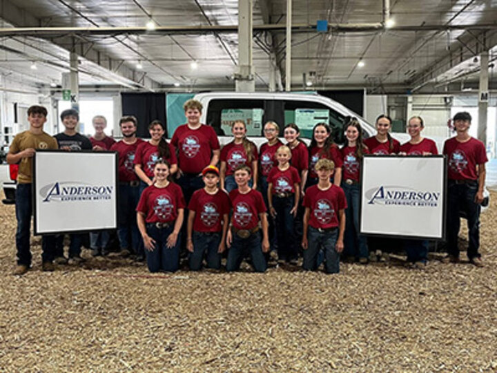 Group of teens in red shirts posing in front of a truck indoors with two “Anderson” signs.