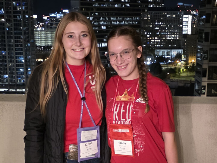 Two teenage women standing in front of a cityscape of downtown skyscrapers during the night