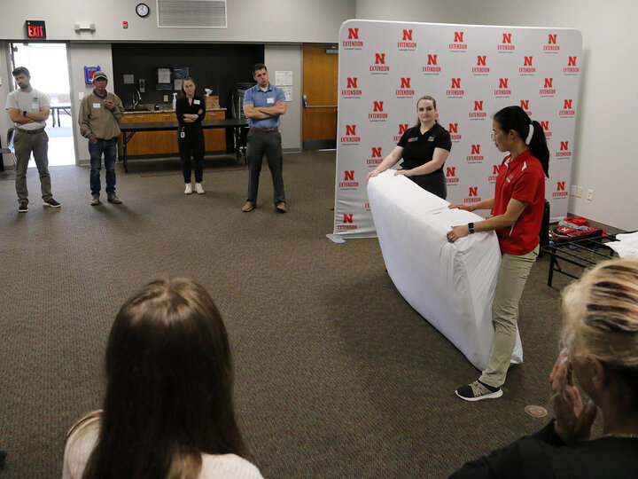 two educators holding a twin size mattress on end, teaching several adults