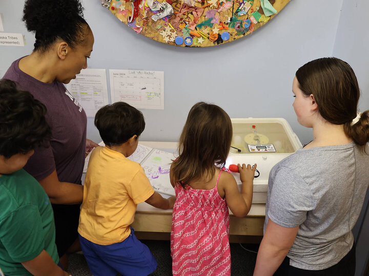 an adult with several young children looking at an incubator with eggs