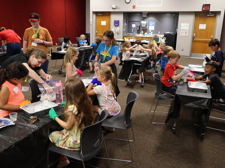 Several youth at tables with adults helping make homemade ice cream with ice in bags