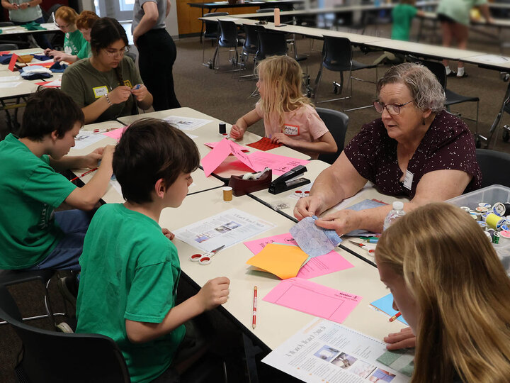 several youth around a table practicing a simple sewing stitch, led by an adult