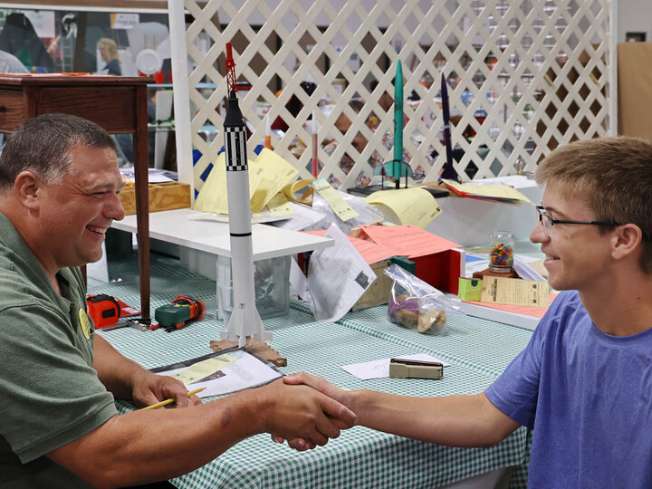 A male judge shaking hands with a boy, rocket models are in the background