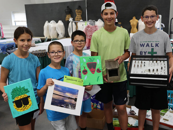 Five siblings at fair holding a variety of exhibits, including artwork and an insect collection