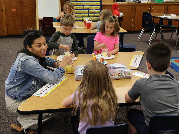 A classroom with an adult and kindergardeners making pudding cups