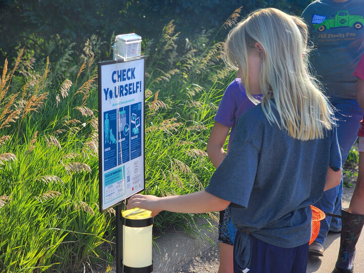 three youth putting something in a container next to a sign that reads "Check Yourself"