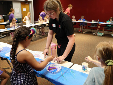 An adult assisting a young child drip an eyedropper of colored water onto a coffee filter