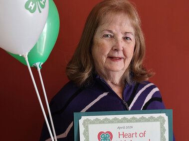 Elderly woman holding two balloons and a certificate that says April 2026 Heart of 4-H Award
