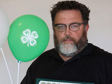 Man holding two balloons with 4-H emblem and a certificate