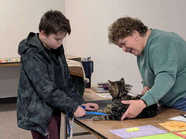 Preteen boy holding a cat on a leash on a table between him and the adult female judge