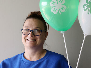 A woman smiling, holding two balloons with 4-H logos