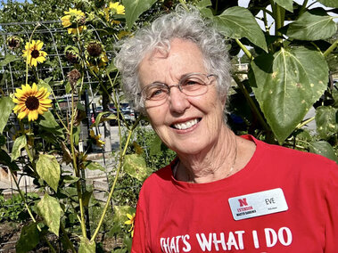 Eve Hoffman with a name tag standing in front tall sunflowers