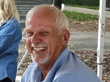 A smiling man outdoors with legs of a tent booth in the background