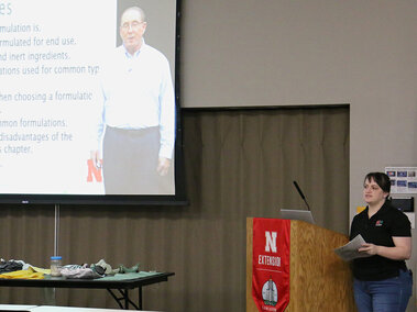 A female presenter standing next to a podium and projection screen