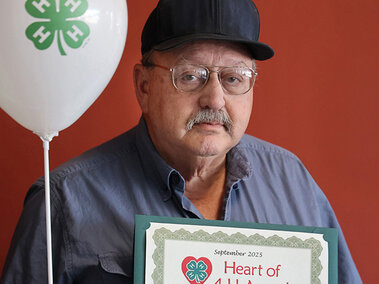 Man holding two balloons with 4-H emblem and a certificate that says Heart of 4-H Award