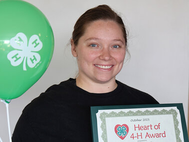 Woman holding a certificate which says "Heart of 4-H Award" and two balloons with 4-H logo