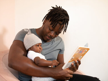Adult male reading a book to a toddler sitting in his lap