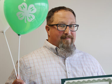 A man holding two balloons with 4-H logos and a certificate saying "Heart of 4-H Award"