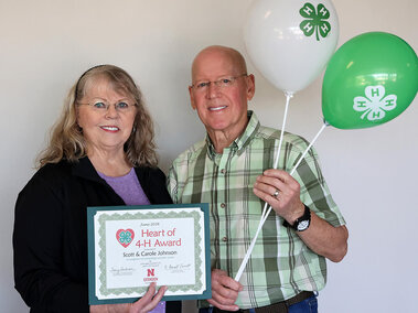 Two people holding a certificate and 4-H branded balloons against a plain background.