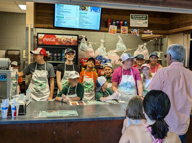 Several youth and two adults at a concession stand, serving people at a window