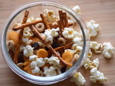 Small bowl of a snack mix including popcorn, round cereal pieces, fish crackers and prezels