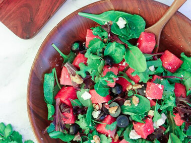 Fresh salad with spinach, watermelon, grapes, walnuts, and feta in a wooden bowl.
