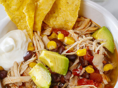 Bowl of soup with shredded chicken, corn, beans - with tortillas sticking out of the soup