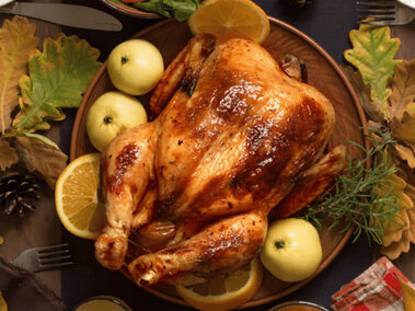 A platter with a baked whole turkey with apples and orange slices