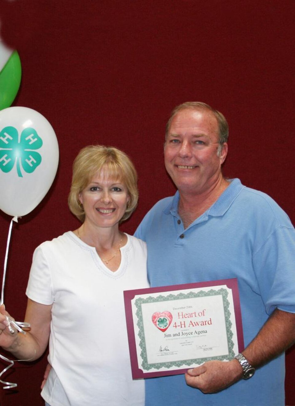 Joyce and Jim Agena standing together and holding balloons and a certificate 