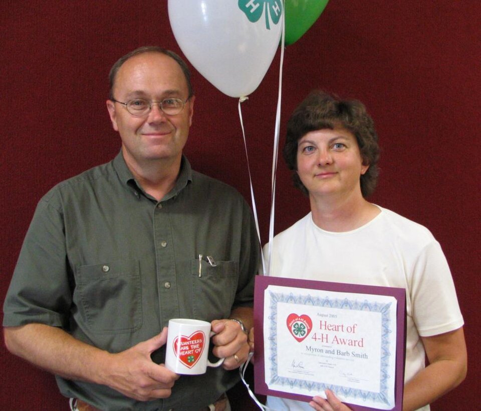 Barb and Myron Smith standing together and holding balloons, a certificate, and a mug 