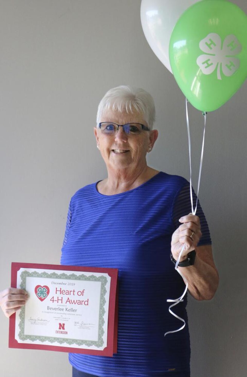 Beverlee Keller holding 4-H balloons and a certificate. 