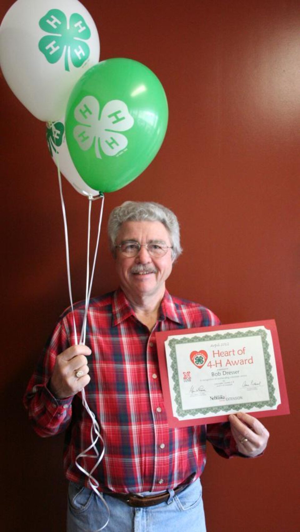 Bob Dresser holding 4-H balloons and a certificate. 