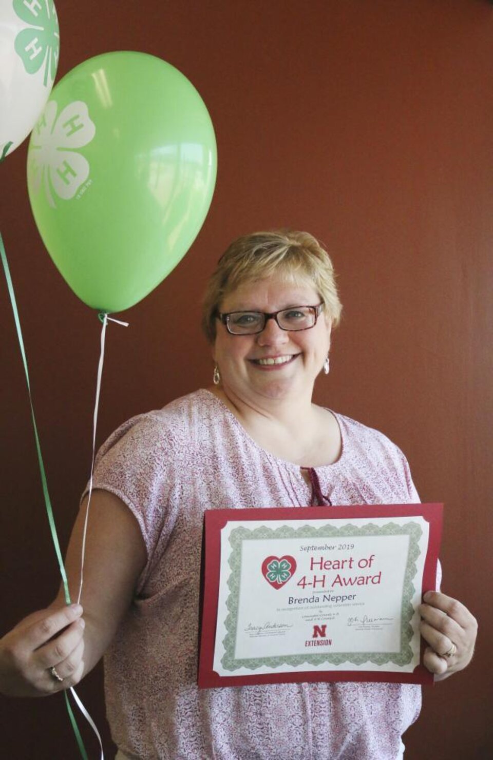 Brenda Nepper holding 4-H balloons and a certificate. 