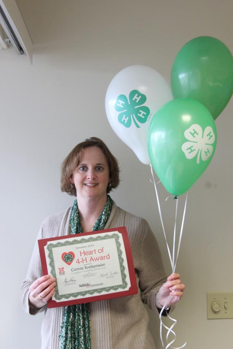 Connie Kreikemeier holding 4-H balloons and a certificate. 