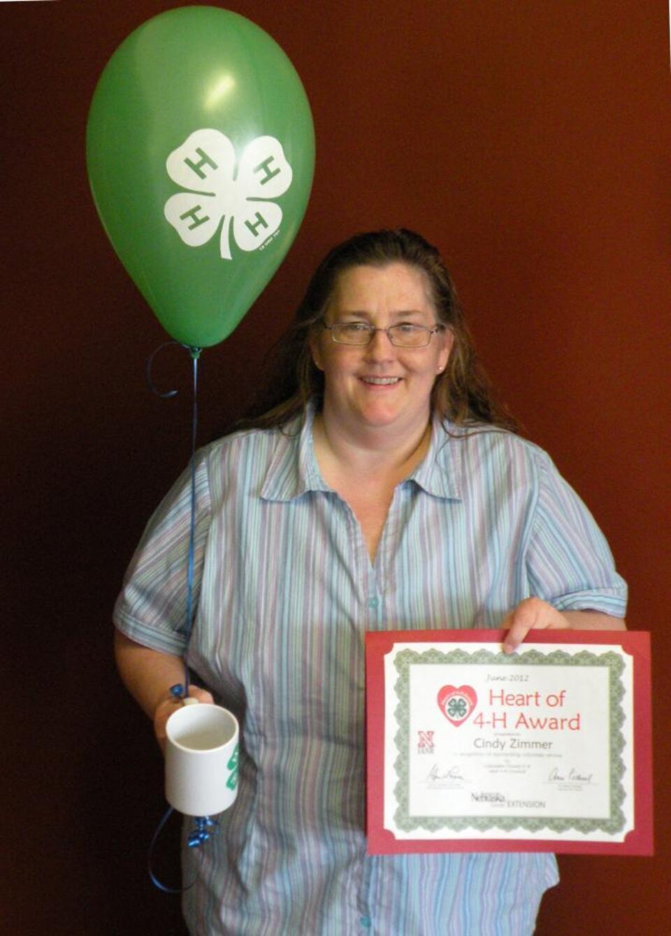 Cindy Zimmer holding a 4-H mug, 4-H balloons, and a certificate. 