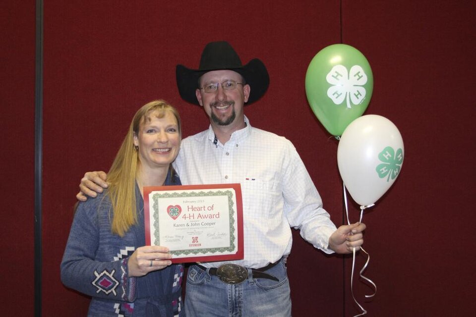 Karen and John Cooper standing together and holding 4-H balloons and a certificate. 