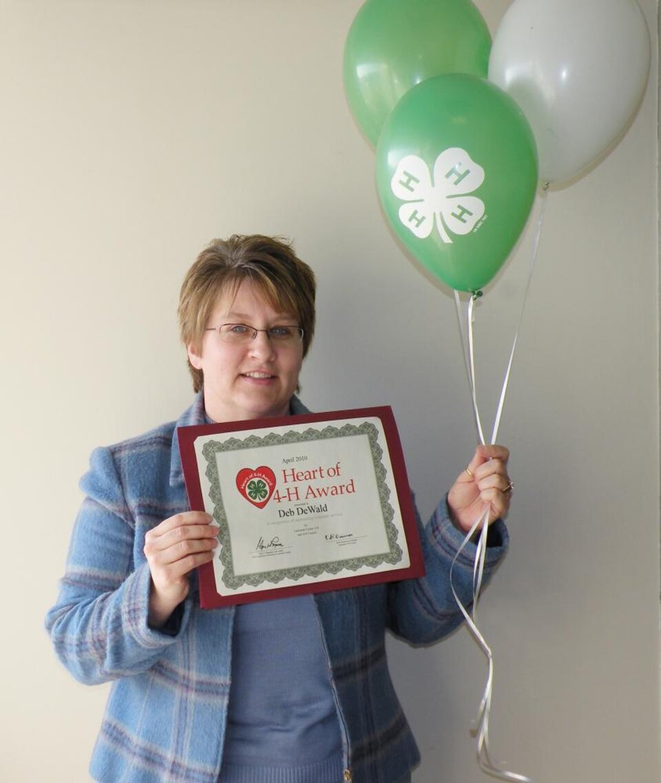 Deb DeWald holding 4-H balloons and a certificate 