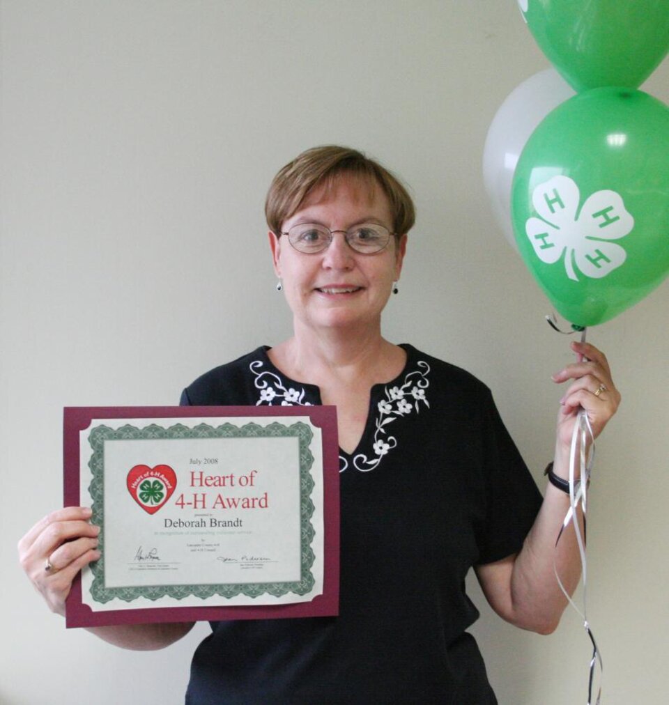 Debbie Brandt holding balloons and a certificate 