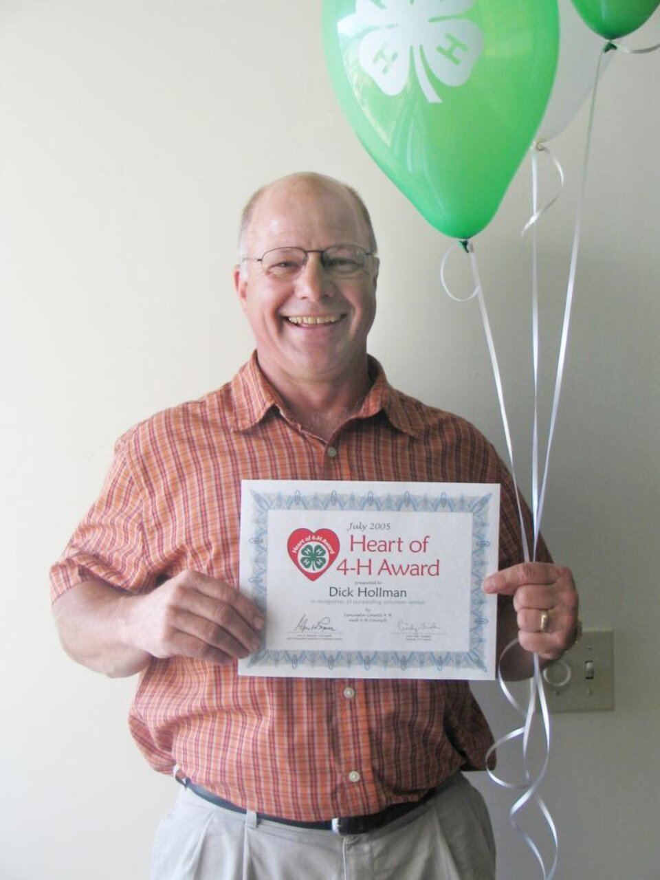 Dick Hollman holding balloons and a certificate 