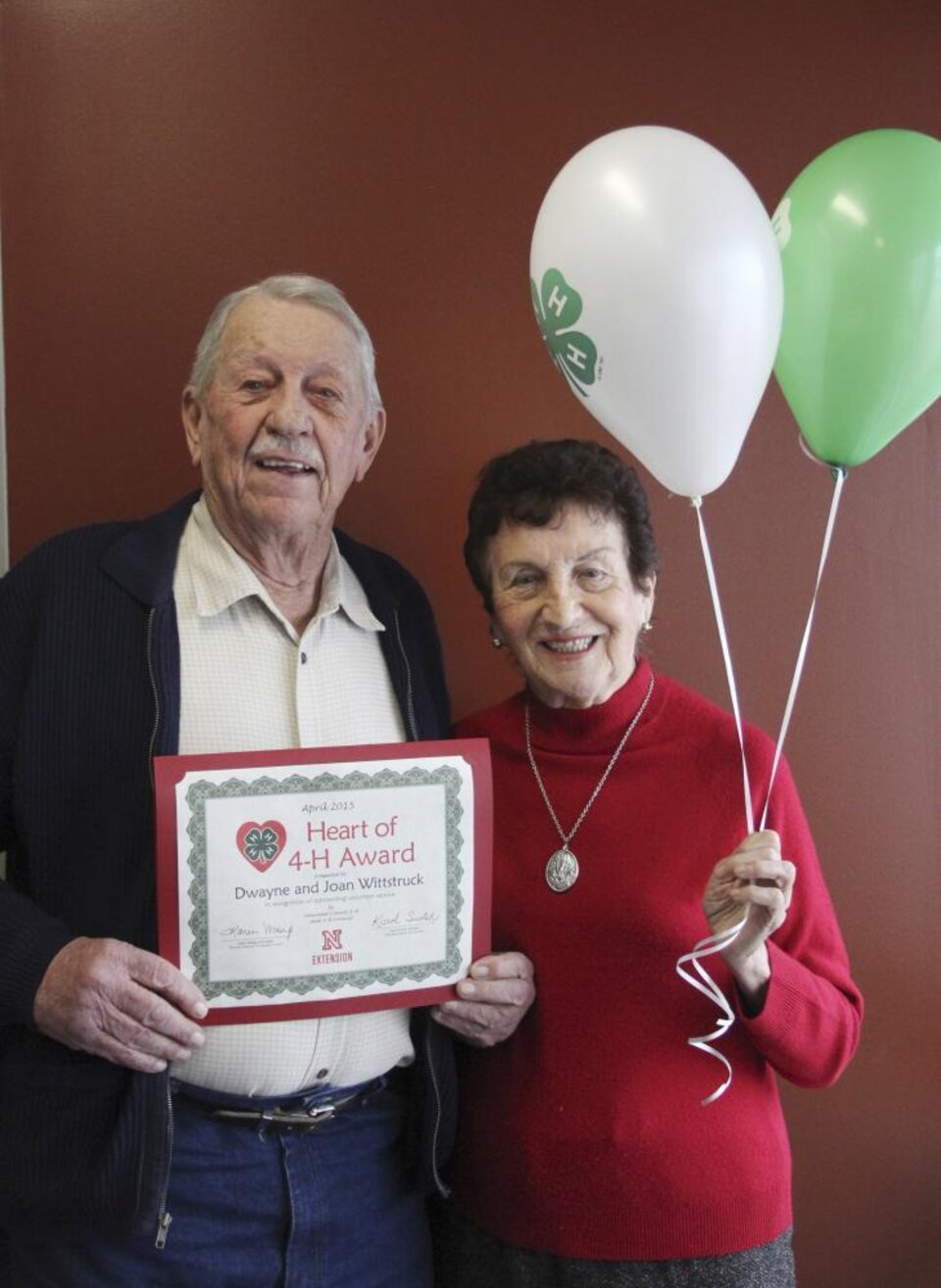 Dwayne and Joan Wittstruck standing together and holding 4-H balloons and a certificate. 