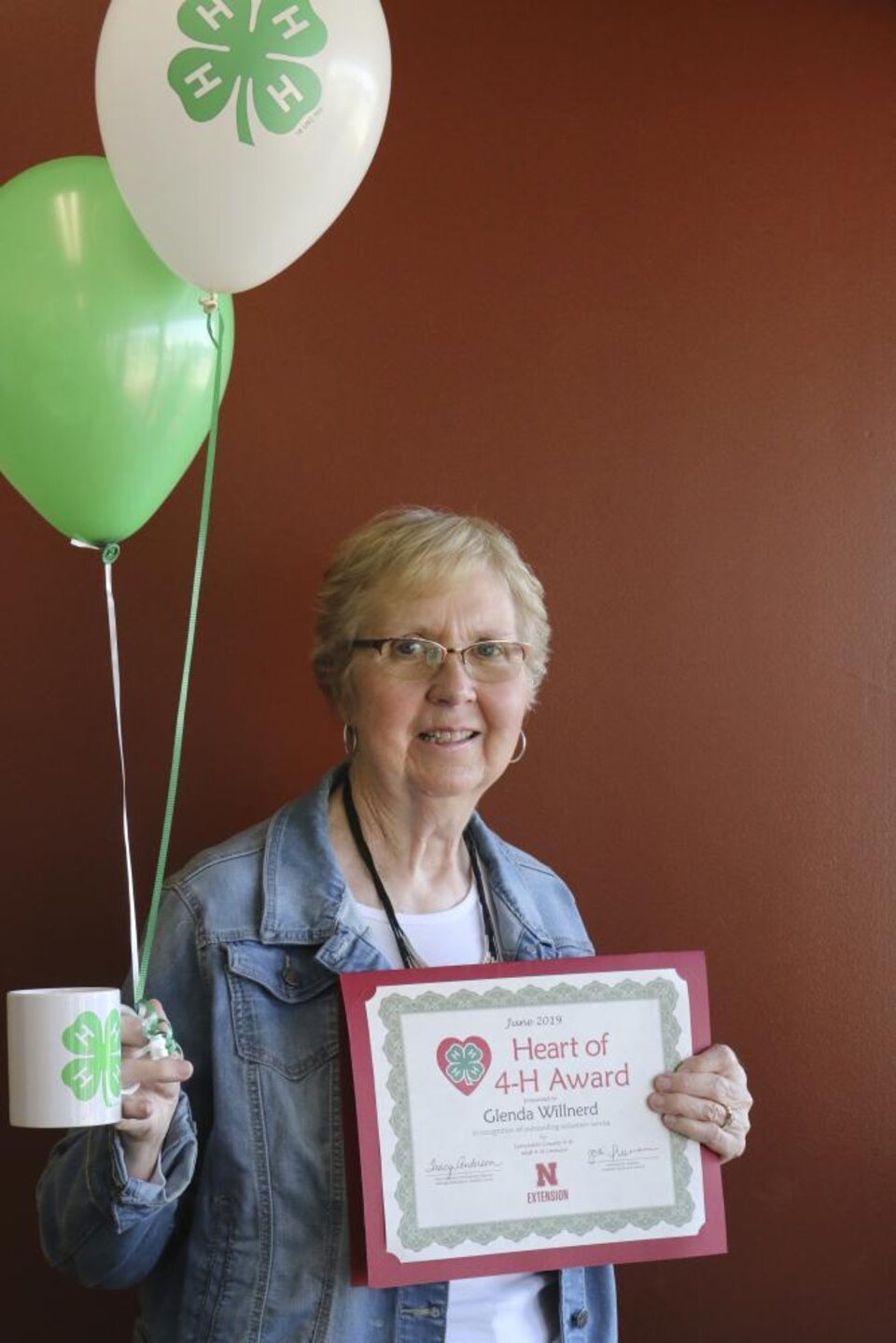 Glenda Willnerd holding 4-H balloons, a 4-H mug, and a certificate. 