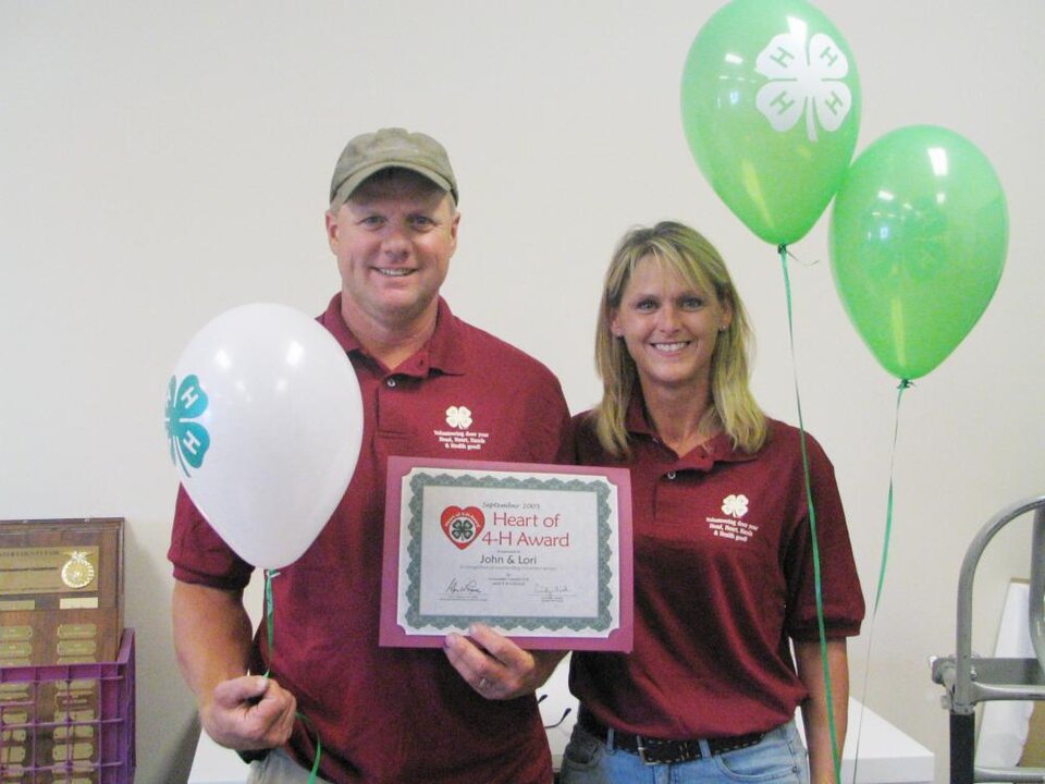 John and Lori Bruss standing next to each other holding balloons and a certificate 