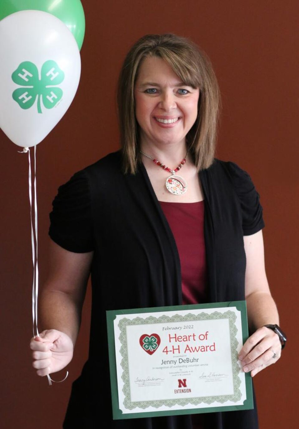 Jenny DeBuhr holding 4-H balloons and a certificate. 