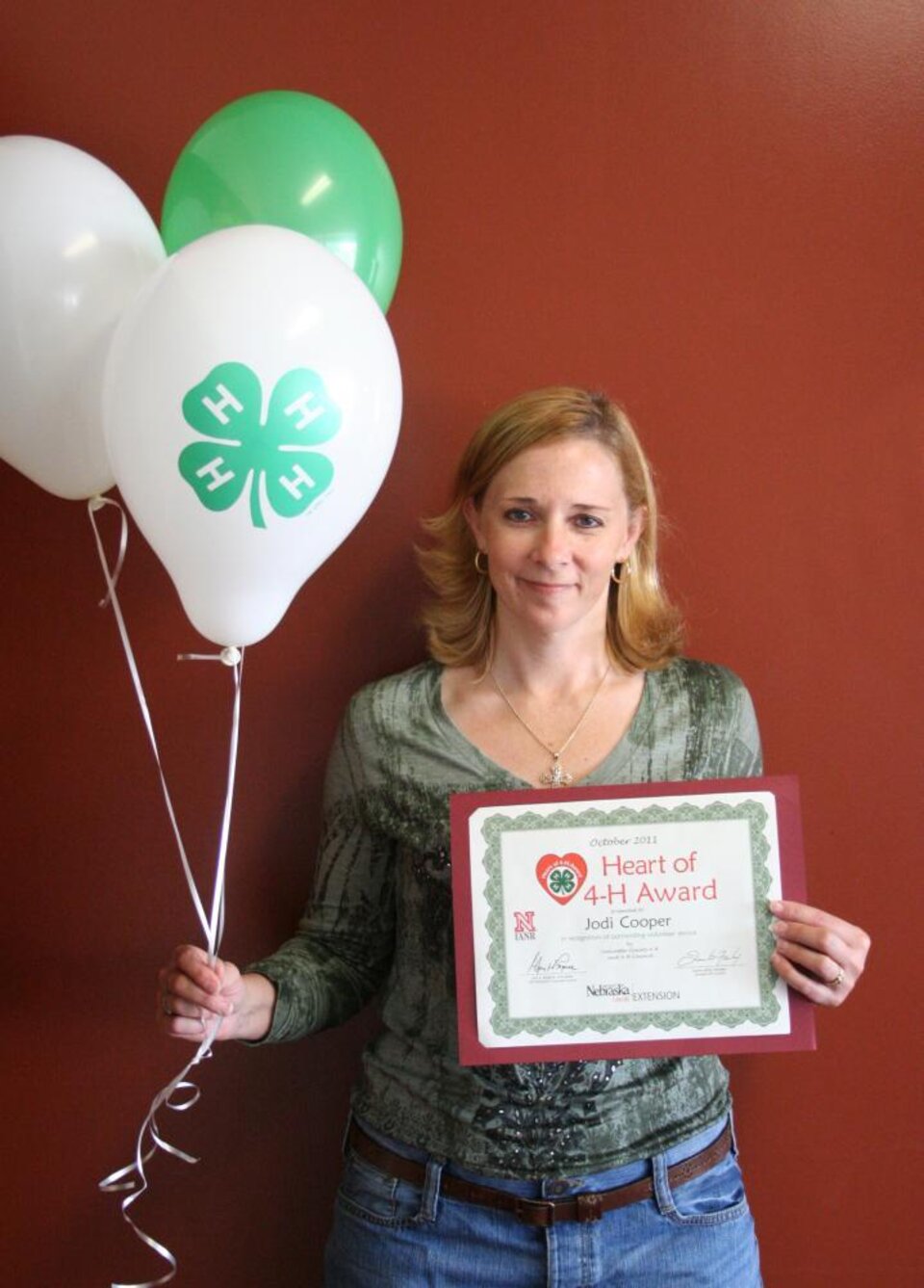 Jodi Cooper holding 4-H balloons and a certificate. 