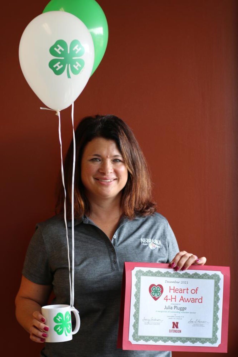 Julia Plugge holding 4-H balloons, a 4-H mug, and a certificate. 