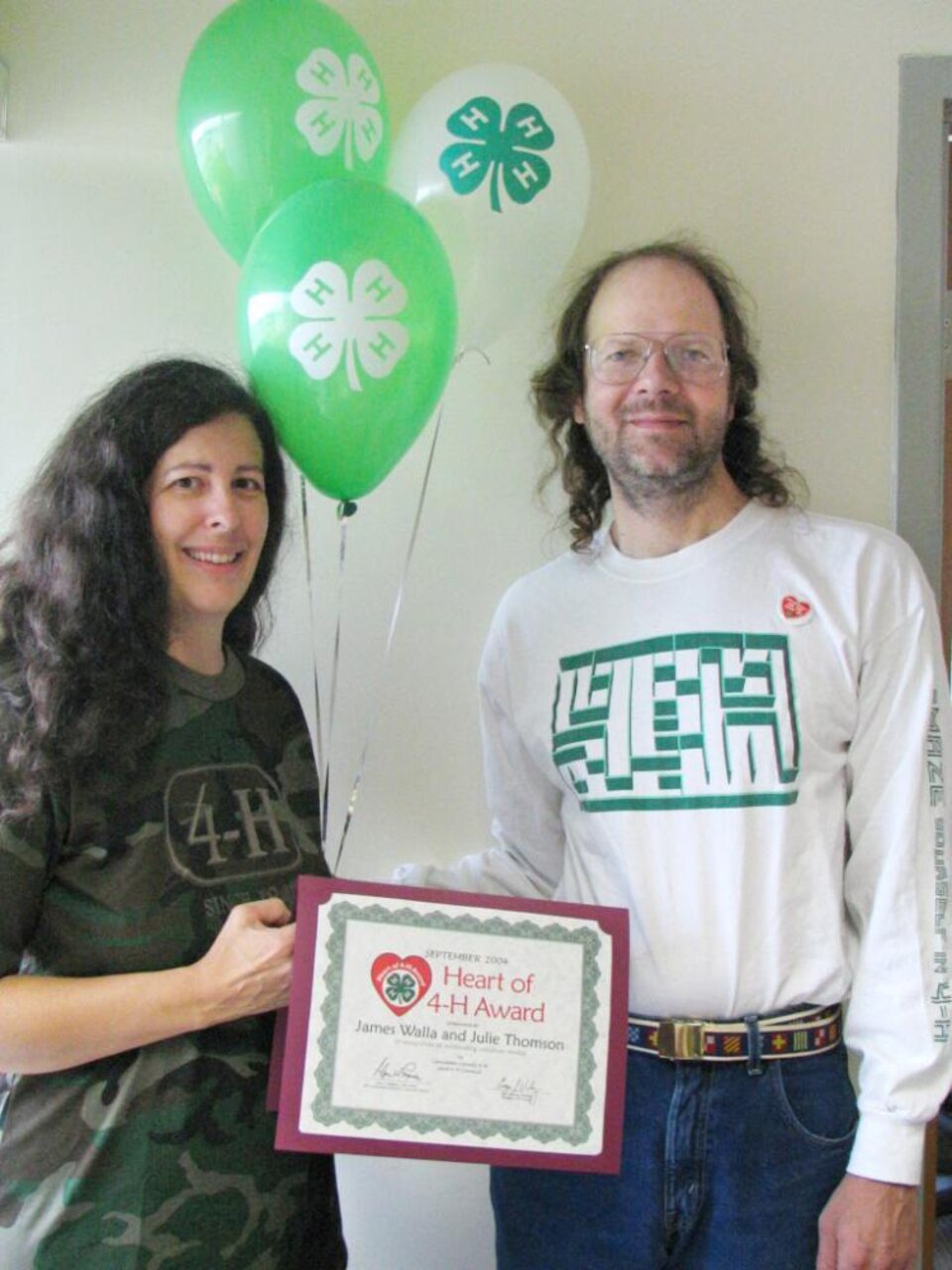 Julie Thomson and James Walla standing together, holding balloons and a certificate 