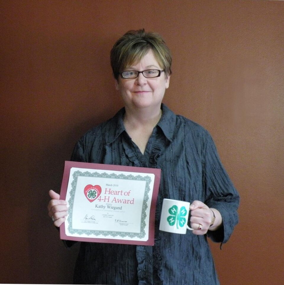 Kathy Wiegand holding a 4-H mug and a certificate. 