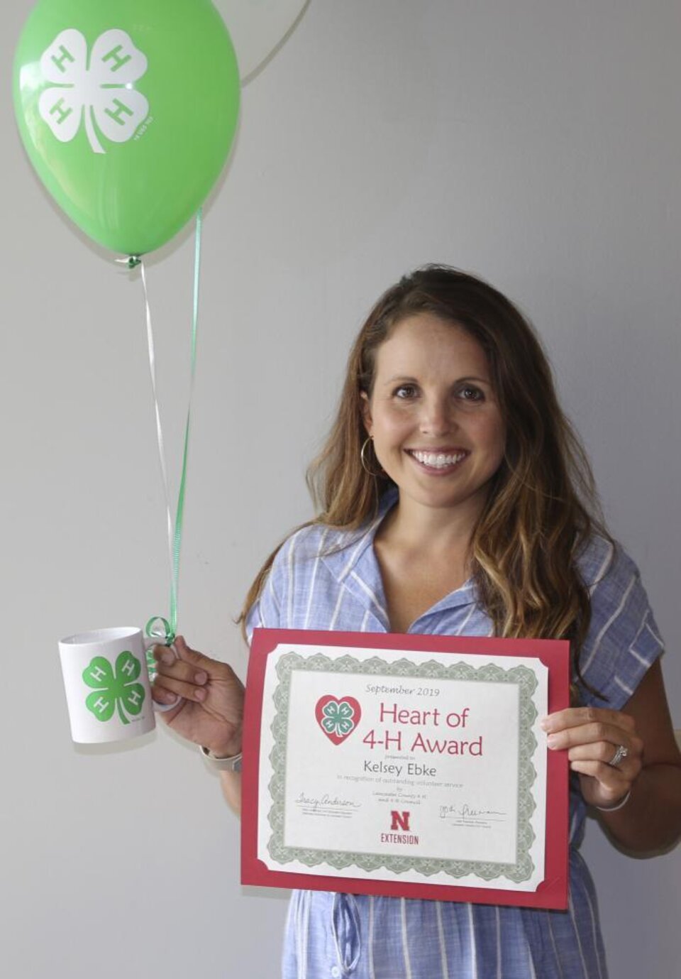 Kelsey Ebke holding 4-H balloons, a 4-H mug, and a certificate. 